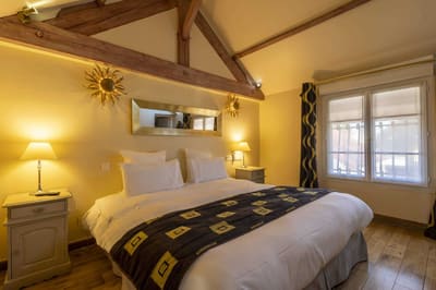 Chambre Amazone : lit sous la charpente, jeté sombre à motifs dorés, miroirs soleil et fenêtre