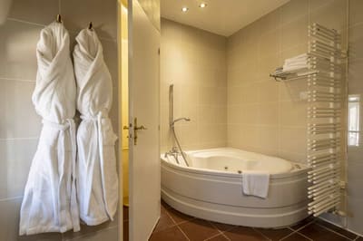 Chambre Amazone : baignoire d’angle, peignoirs blancs et sèche-serviettes, carrelage beige
