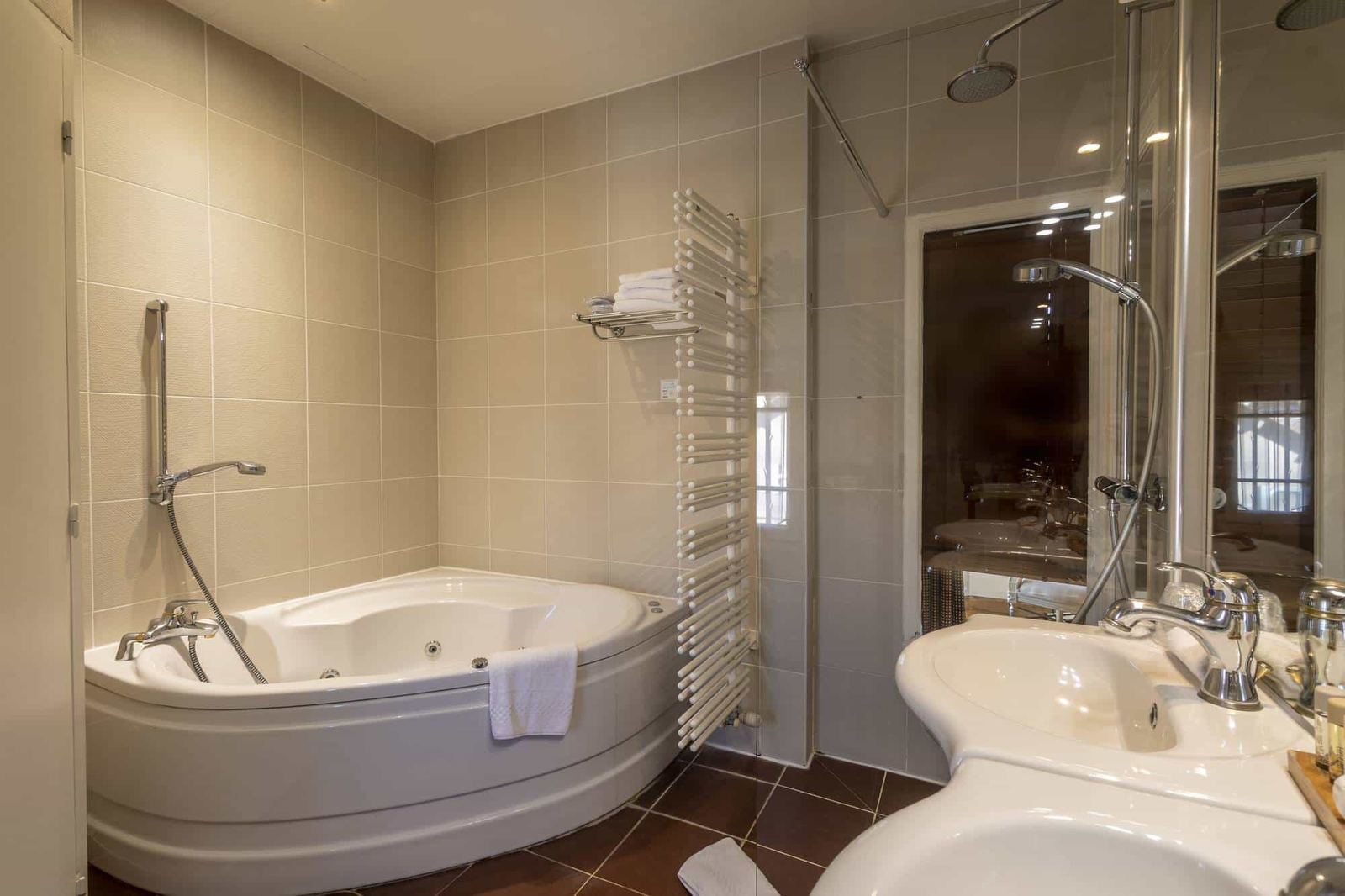 Chambre Amazone : baignoire d’angle, sèche-serviettes blanc, douche vitrée et vasque, sol brun