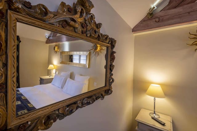 Chambre Amazone : miroir baroque doré reflétant le lit et sa lampe de chevet