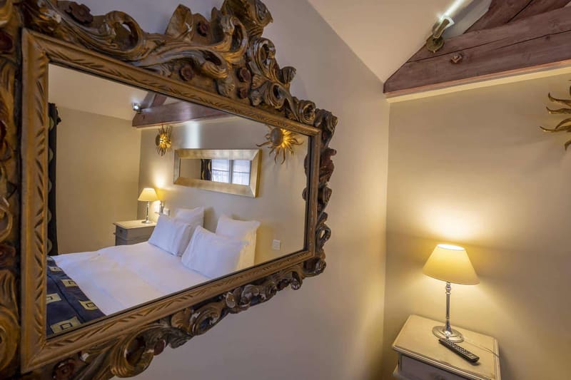 Chambre Amazone : miroir baroque doré reflétant le lit et sa lampe de chevet