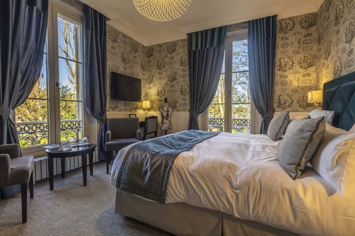 Chambre Bleue : tête de lit bleu canard, rideaux bleus et grandes fenêtres sur les arbres