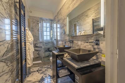 Chambre Bleue : salle de bains en marbre, douche vitrée, double vasque noire et miroir éclairé