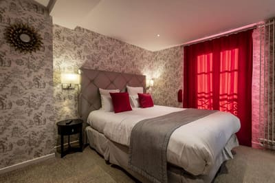 Chambre Coquelicot : lit à tête capitonnée, coussins et rideaux rouges, toile de Jouy