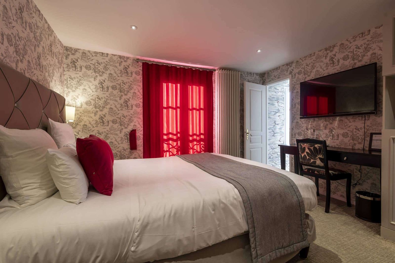 Chambre Coquelicot : lit, rideaux rouges, bureau et porte ouverte sur la salle de bains en marbre