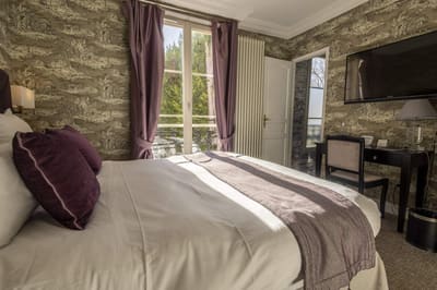 Chambre Coquillage : lit aux coussins prune, rideaux mauves et fenêtre sur les arbres
