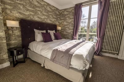 Chambre Coquillage : lit capitonné prune, rideaux mauves et fenêtre à balcon sur les arbres