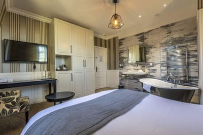 Chambre Coquine : lit, armoire blanche, bureau et baignoire sur pieds dans l’alcôve en marbre