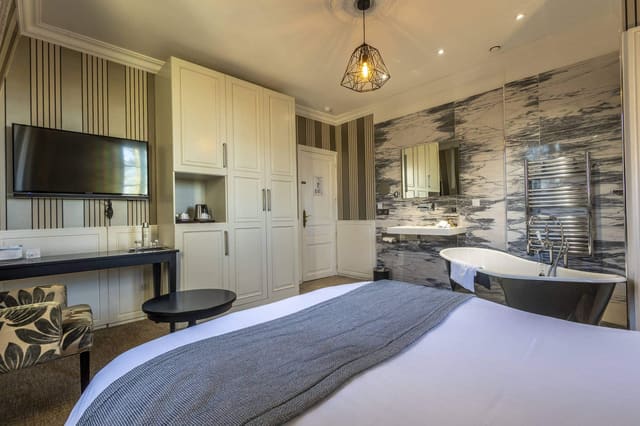 Chambre Coquine : lit, armoire blanche, bureau et baignoire sur pieds dans l’alcôve en marbre