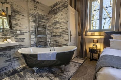 Chambre Coquine : baignoire sur pieds noire dans le marbre veiné, fenêtre sur les arbres