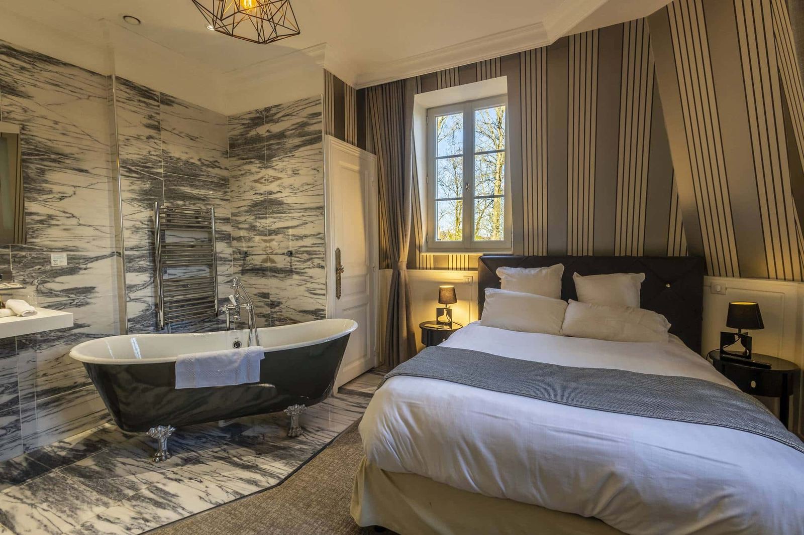 Chambre Coquine : lit à tête capitonnée, baignoire sur pieds noire et marbre gris veiné