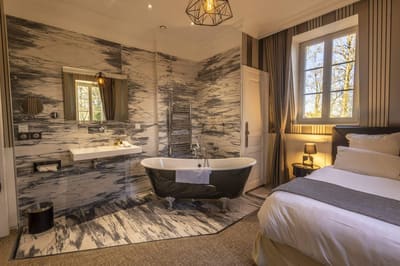 Chambre Coquine : vasque, baignoire sur pieds et lit sous une suspension géométrique dorée