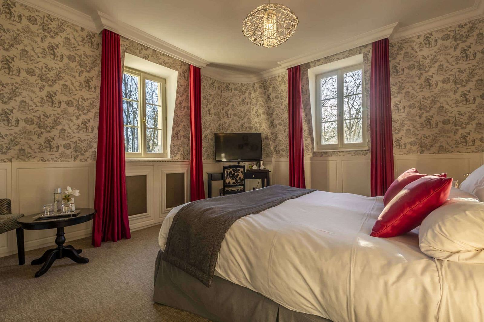 Chambre Dorée : lit à coussins rouges, toile de Jouy et deux fenêtres aux rideaux assortis