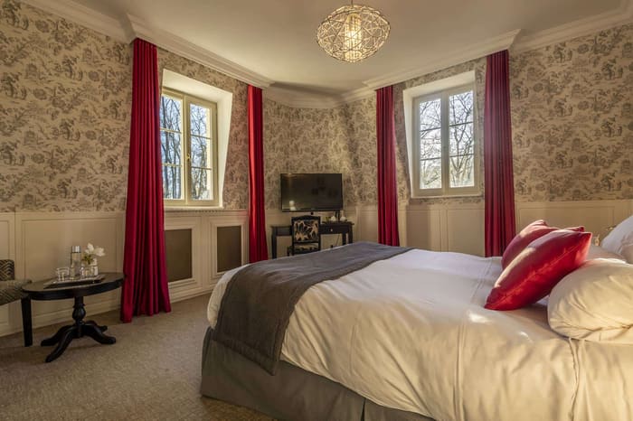 Chambre Dorée : lit à coussins rouges, toile de Jouy et deux fenêtres aux rideaux assortis