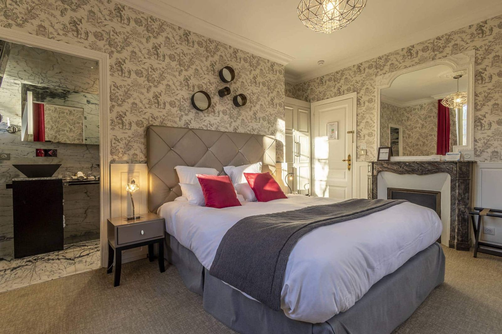Chambre Dorée : lit capitonné aux coussins rouges, cheminée de marbre et salle de bain ouverte