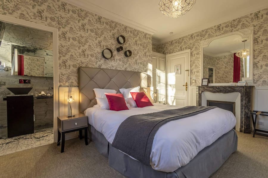 Chambre Dorée : lit capitonné aux coussins rouges, cheminée de marbre et salle de bain ouverte