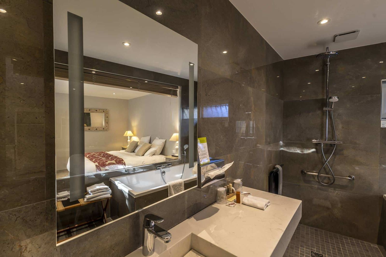 Chambre Centaure : miroir éclairé reflétant la baignoire et le lit, vasque et douche à l’italienne