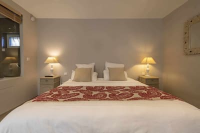 Chambre Centaure : lit blanc au chemin de lit rouge, coussins beiges et lampes de chevet
