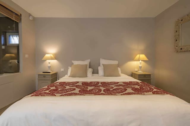Chambre Centaure : lit blanc au chemin de lit rouge, coussins beiges et lampes de chevet