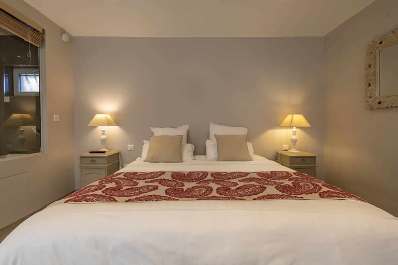 Chambre Centaure : lit blanc au chemin de lit rouge, coussins beiges et lampes de chevet