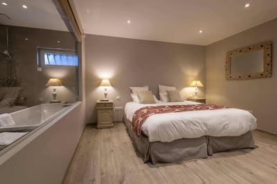Chambre Centaure : lit au chemin de lit rouge, murs taupe, baignoire derrière la paroi vitrée