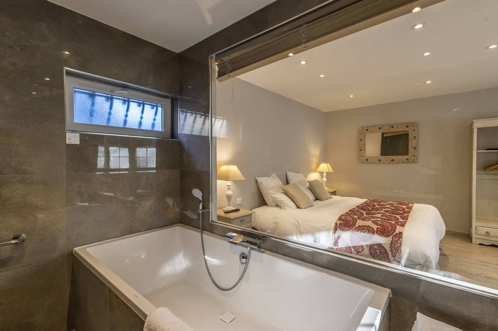 Chambre Centaure : baignoire blanche et carrelage sombre, grande vitre ouverte sur le lit