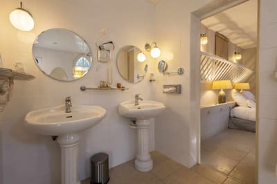 Chambre Poulinière : deux lavabos sur colonne, miroirs ronds et carrelage blanc, ouverture sur le lit
