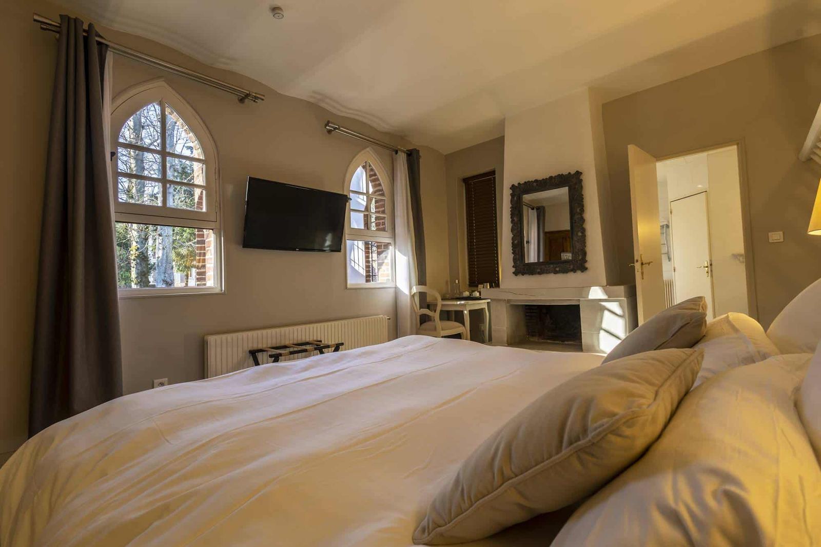 Chambre Poulinière : depuis le lit, fenêtres en ogive sur les arbres, télévision et cheminée