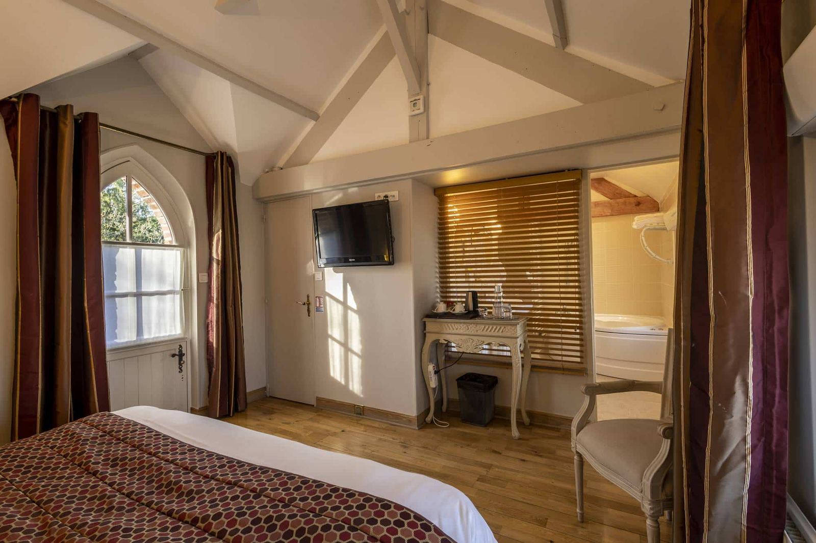 Chambre Voltige : charpente apparente, fenêtre en ogive, parquet et baignoire d’angle entrevue
