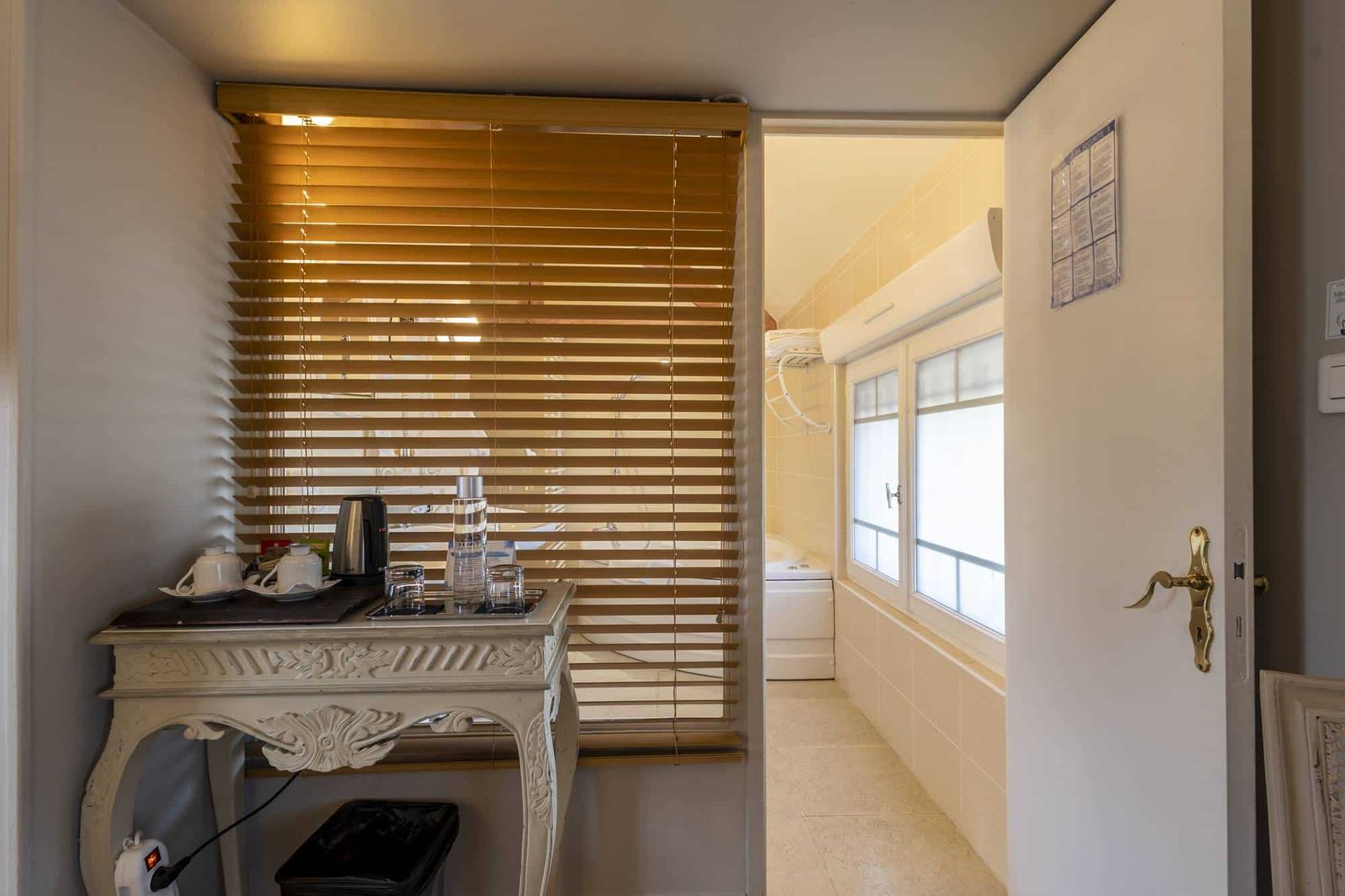 Chambre Voltige : console sculptée blanche à bouilloire, store en bois et salle de bain crème