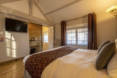 Chambre Voltige : lit sous les poutres, parquet, plaid à motifs et fenêtre aux rideaux bordeaux