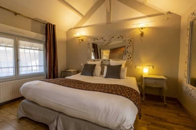 Chambre Voltige : lit vu de face sous les poutres, miroir baroque blanc et appliques allumées