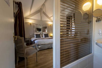 Chambre Voltige : lit sous la charpente, miroir baroque blanc, fauteuil canné et parquet