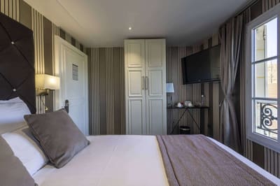 Chambre Vue sur Ferme : lit capitonné, armoire blanche et fenêtre ouverte au garde-corps en fer forgé