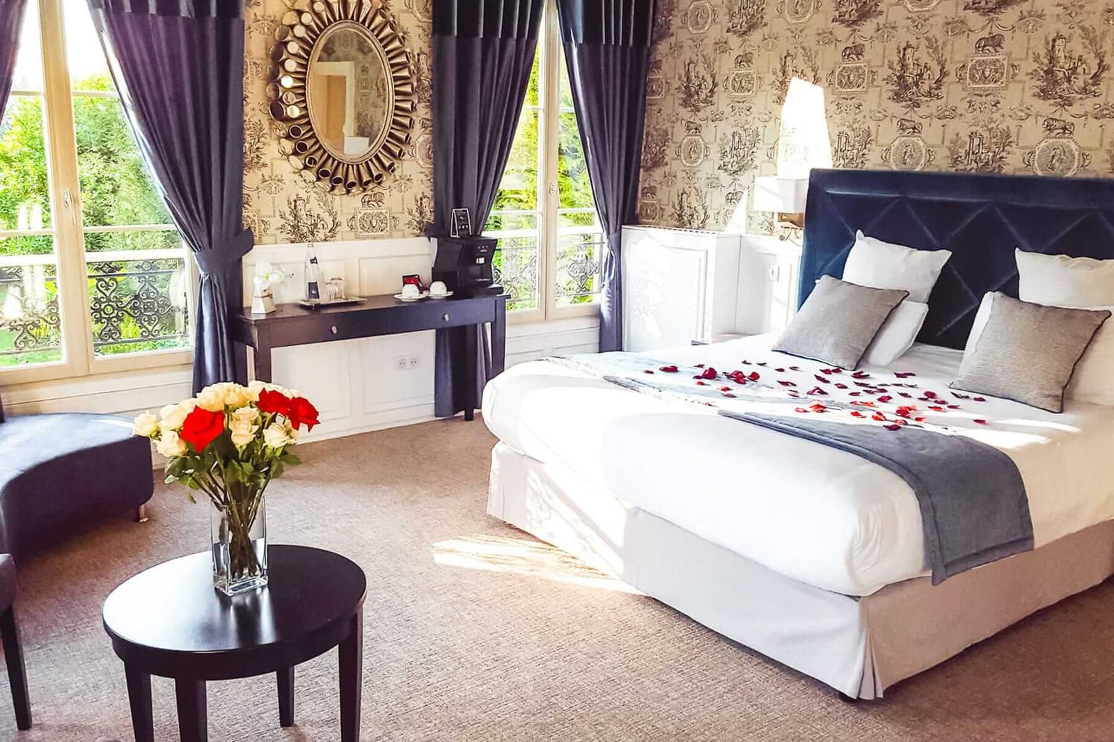 Suite Marquise : lit à tête bleu nuit, pétales de rose, bouquet et fenêtres sur la verdure