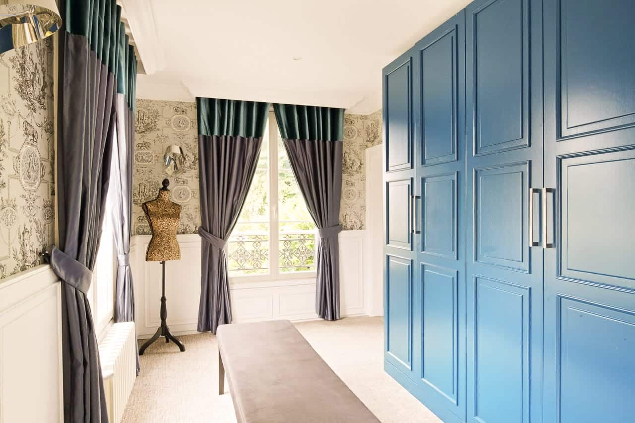Suite Marquise : grands placards bleus, banquette grise et fenêtre à balconnet sur la verdure