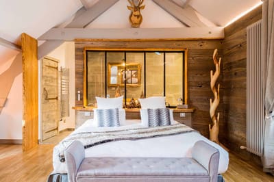 Suite Megève : lit blanc au plaid fourrure, tête de lit en vieux bois et verrière noire