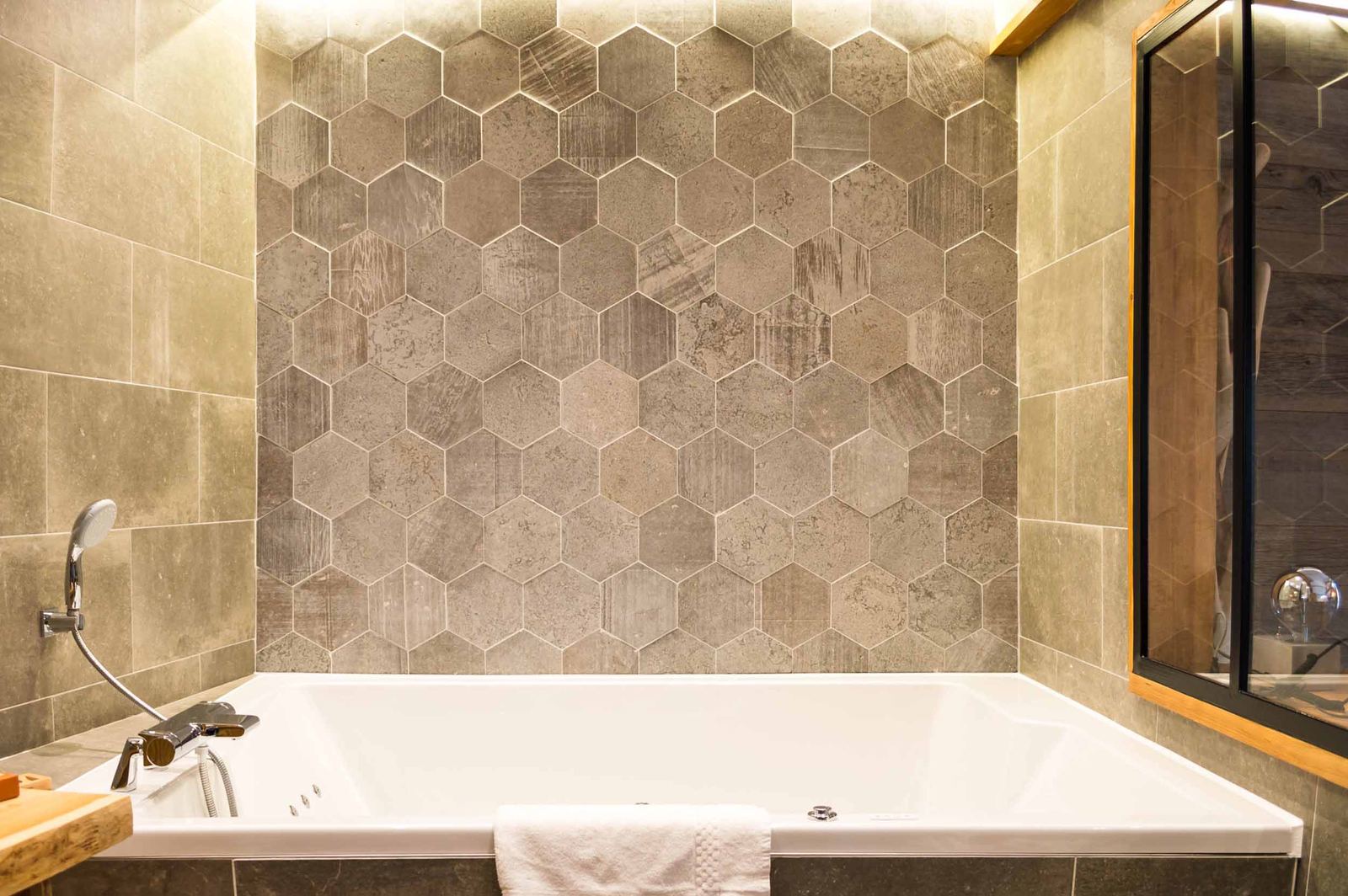 Suite Megève : jacuzzi encastré sous un mur de carreaux hexagonaux gris et verrière