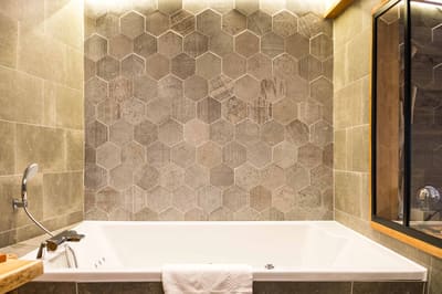 Suite Megève : jacuzzi encastré sous un mur de carreaux hexagonaux gris et verrière
