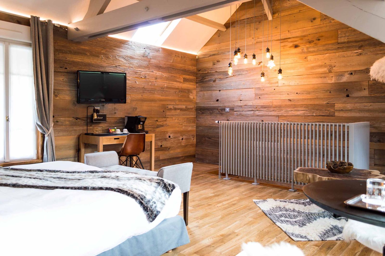 Suite Megève : lit au plaid fourrure, bureau avec télévision et mur de vieux bois