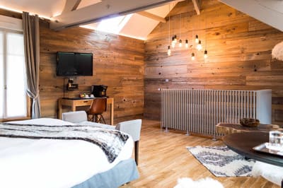 Suite Megève : lit au plaid fourrure, bureau avec télévision et mur de vieux bois