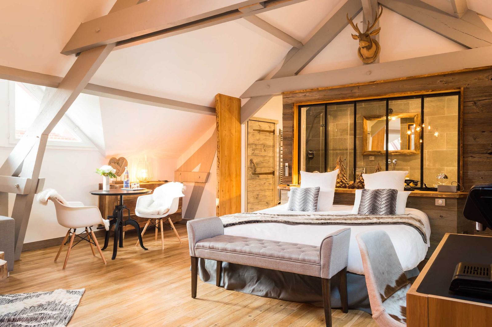 Suite Megève : chambre sous charpente, lit, banquette et coin salon aux fauteuils blancs