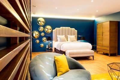 Suite Océan : canapé arrondi et coussin jaune devant le lit, murs bleu nuit et miroirs dorés