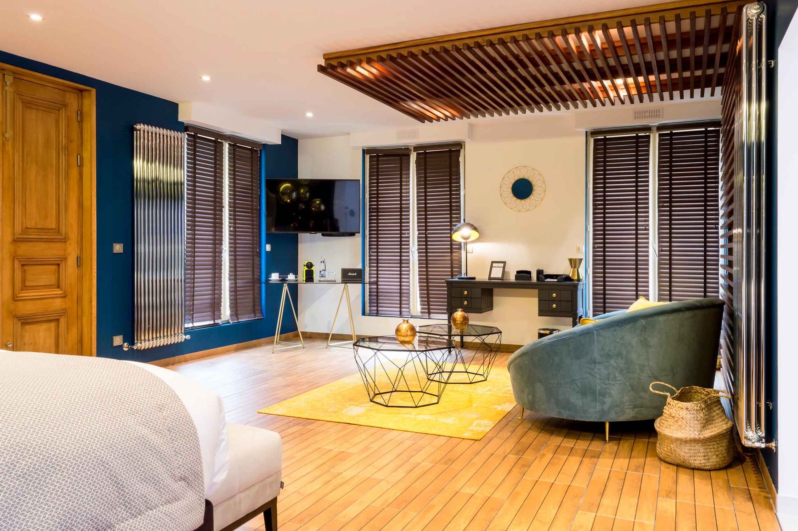 Suite Océan : salon au canapé bleu canard, tapis jaune, bureau et stores de bois