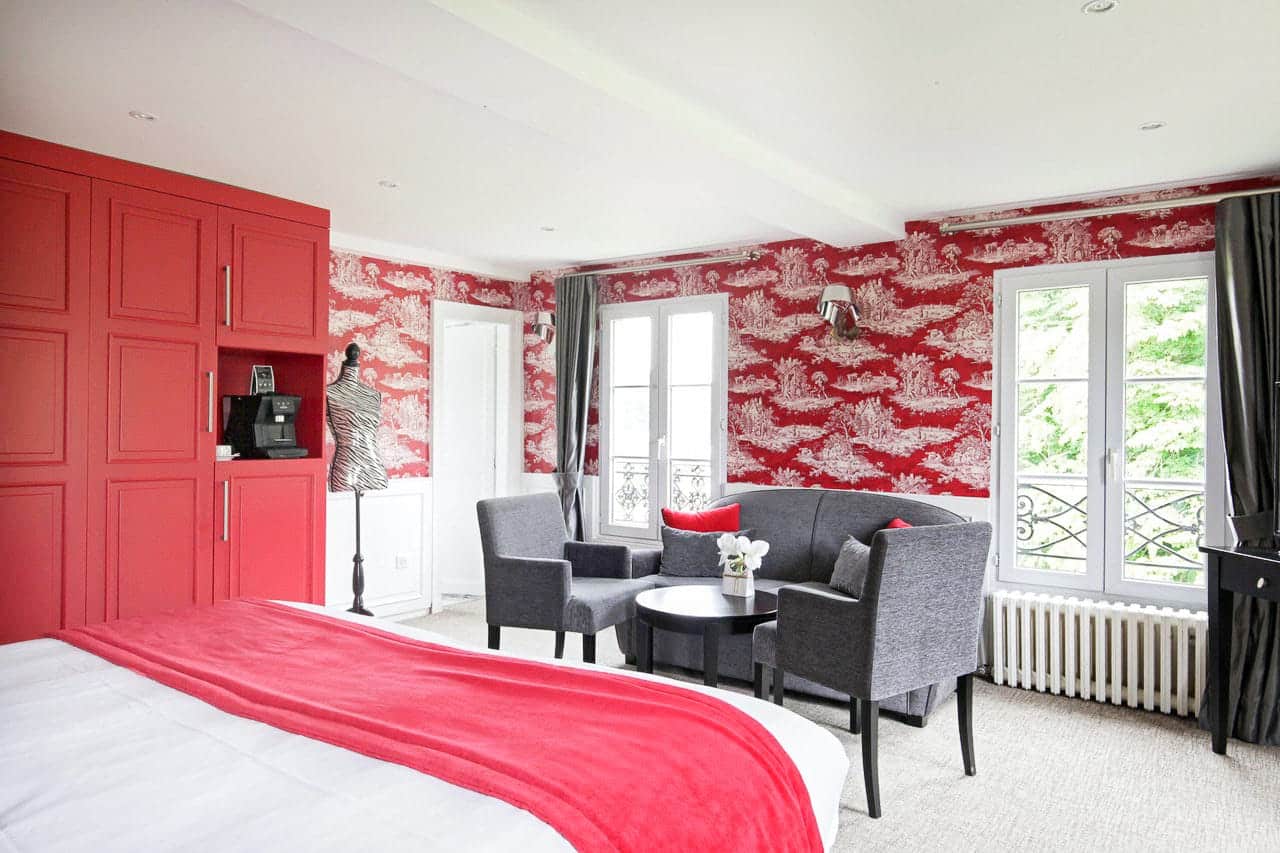 Suite Arlequin : placards rouges, coin salon gris et fenêtres à balconnet sur les arbres