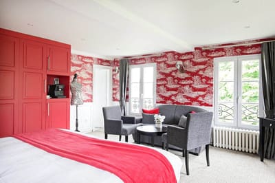 Suite Arlequin : placards rouges, coin salon gris et fenêtres à balconnet sur les arbres