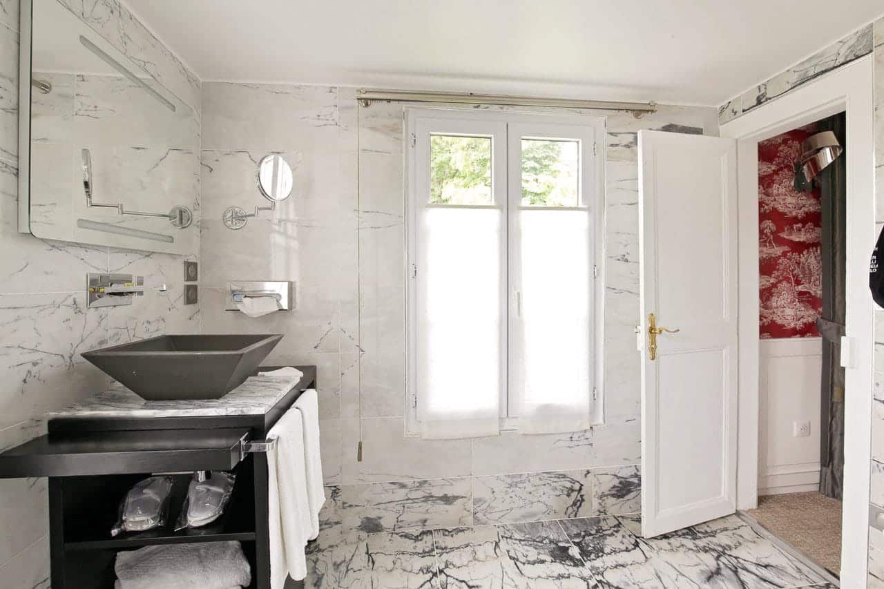 Suite Arlequin : vasque noire sur meuble noir, murs de marbre veiné et fenêtre à voilage