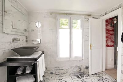 Suite Arlequin : vasque noire sur meuble noir, murs de marbre veiné et fenêtre à voilage