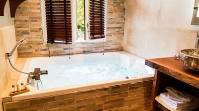 Suite Indonésienne : jacuzzi en bulles sous la fenêtre aux stores de bois et vasque en pierre