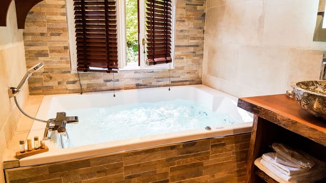 Suite Indonésienne : jacuzzi en bulles sous la fenêtre aux stores de bois et vasque en pierre